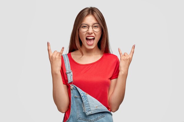 Charismatic woman with appealing look, shows rock n roll gesture, exclaims with pleasure