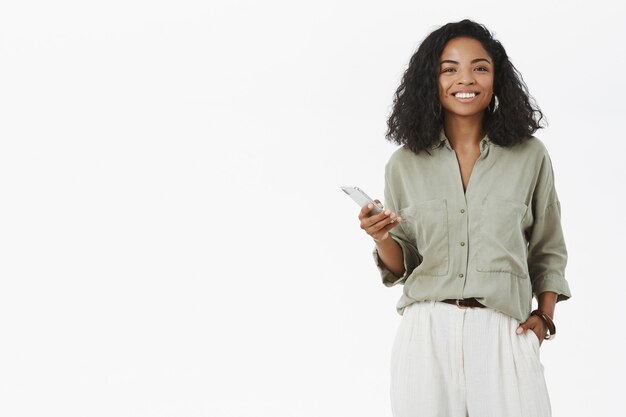 charistmatic charming african american woman with curly hairstyle holding hand in pocket using smartphone