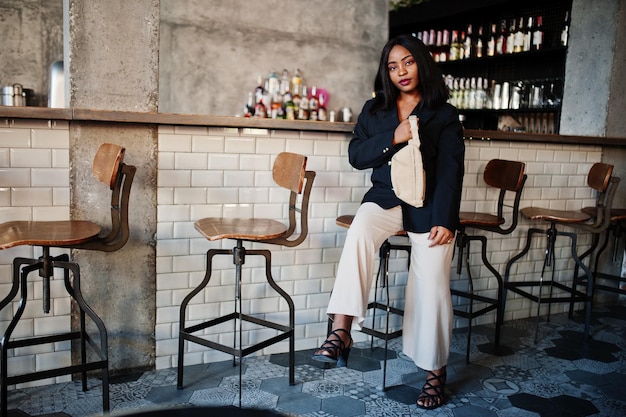 黒のジャケットとウエストバッグの魅力的なアフリカ系アメリカ人女性モデルは、自由時間中にカフェでリラックス