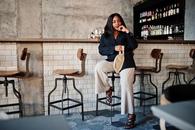 Charming african american woman model in black jacket and waist bag relaxing in cafe during free time