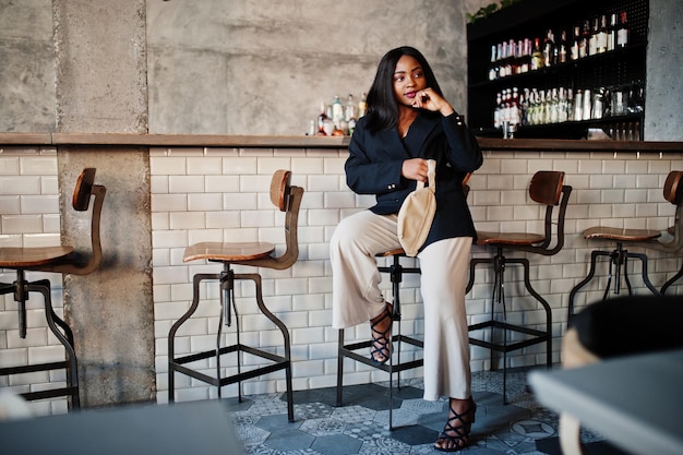 Charming african american woman model in black jacket and waist bag relaxing in cafe during free time