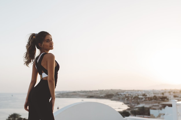 Free photo charming attractive young woman enjoying sunrise on seafront. outwork, sportive lifestyle, fashionable model, time for fitness, looking, cheerful mood.