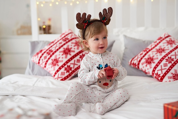 Очаровательная малышка открывает рождественский подарок в постели