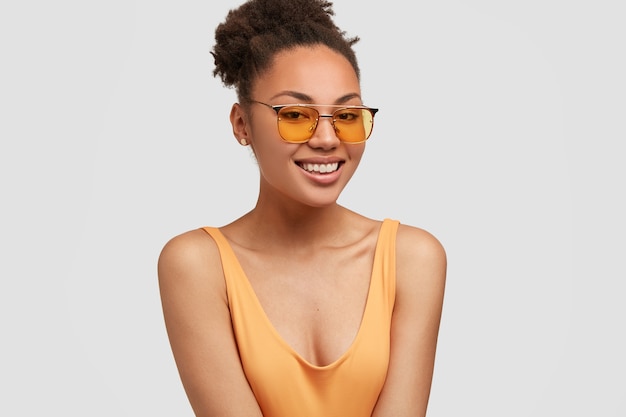 Charming black woman has tender smile, sunglasses, curly hair, dressed in casual clothes