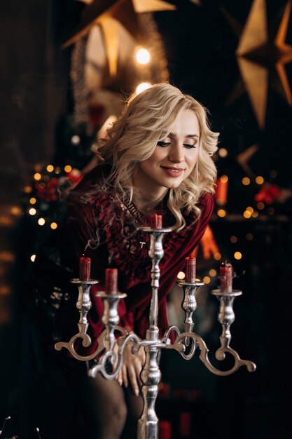 Charming blonde woman looks at candles standing in the room with beautiful Christmas decor