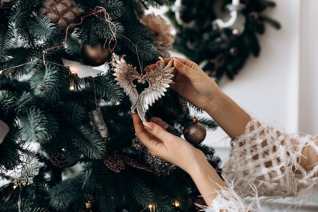 Charming blonde woman in white dress poses in a room with large Christmas tree