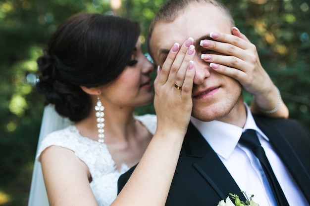 Charming bride closes eyes to her husband (from behind)