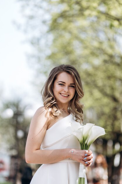 The charming bride keeps a wedding bouquet and stands on the street