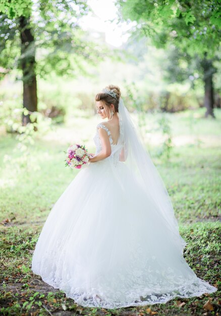 Charming bride poses with colorful wedding bouquet in the park