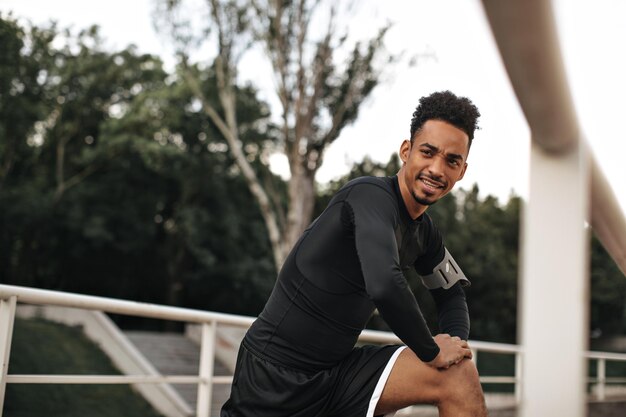 Charming brunet cool man in longsleeved black tshirt looks away and stretches in park Cool guy working out