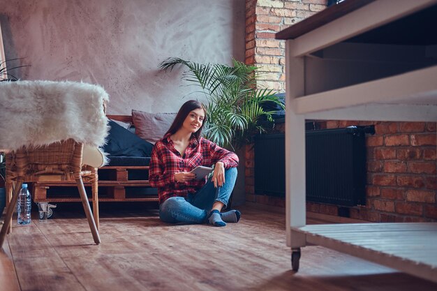 Charming brunette in a flannel shirt and jeans sitting on a floo