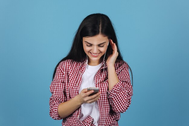 Charming brunette listens to the music in her earphones holding a smartphone