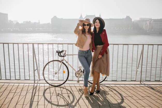 Charming brunette woman in skirt posing with female friend in jeans