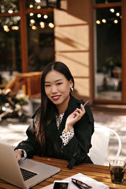 Charming brunette woman with bright lips smiles widely and holds pen