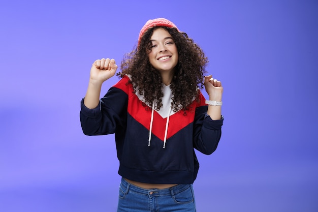 Charming carefree young s girl with curly haircut in warm beanie dancing and having fun joyfully ove...