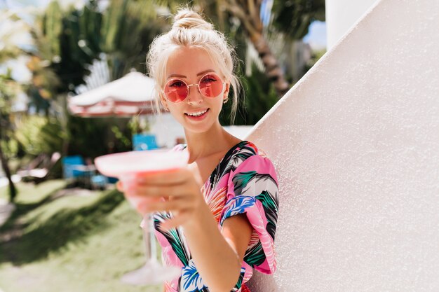 Charming caucasian female model with tanned skin raising glass of cocktail.