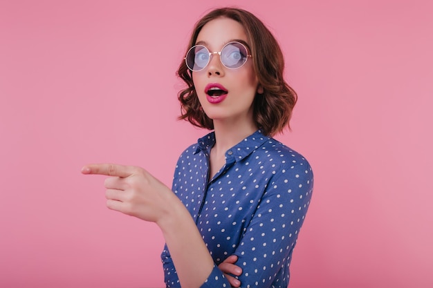 Free photo charming caucasian girl with wavy hairstyle posing on pink background with interested face expression indoor shot of surprised blithesome young woman in sunglasses