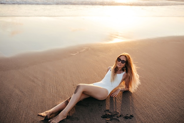 休暇中に砂浜でポーズをとる流行のイヤリングの魅力的な白人女性。