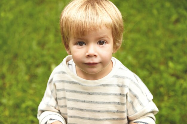 Charming close-up innocent portrait of little innocent kid. Calm Caucasian boy with blond hair, round brown eyes