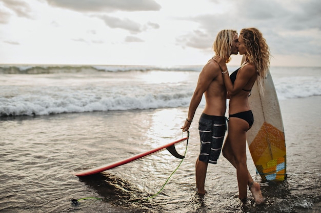 Charming couple of lovers kisses and hugs after surfing