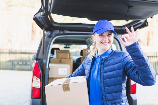 Charming courier with box gesturing at camera