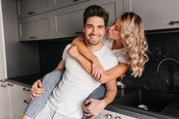 Charming curly girl kissing boyfriend. Amazing fair-haired young woman embracing husband.