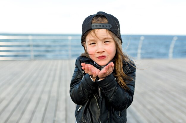 Charming cute little girl dressed in stylish jacket and cap sends a kiss