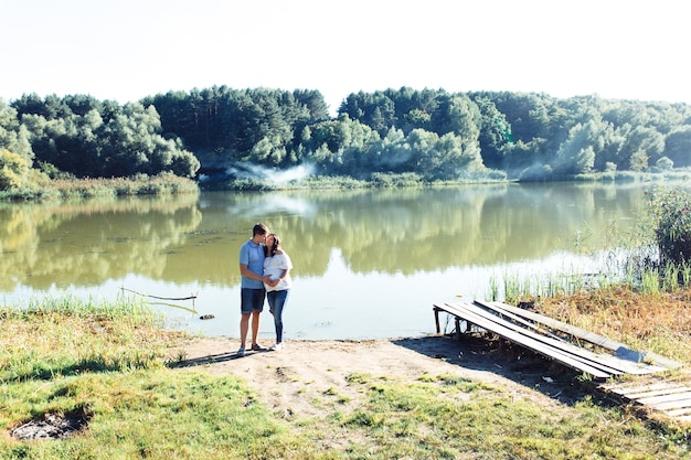 Очаровательная ожидающая пара стоит обниматься зеленой рекой