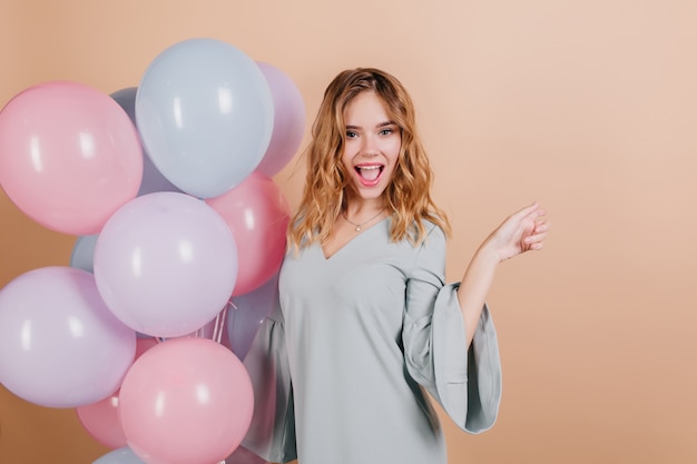 Charming fair-haired birthday woman posing with pleasure on light wall