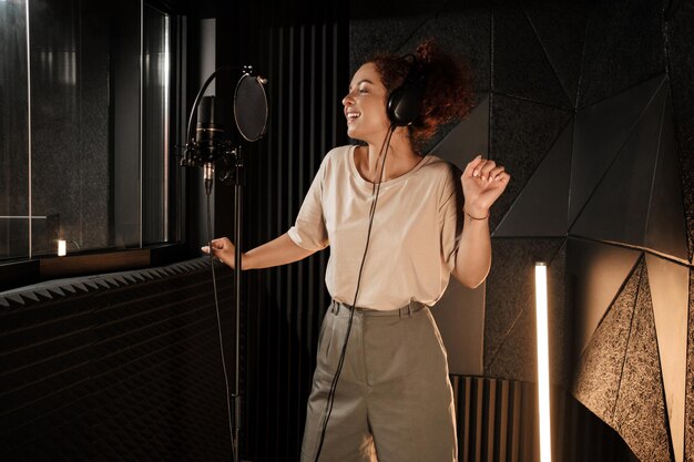 Charming female musician in headphones dreamily dancing while recording song in modern sound studio