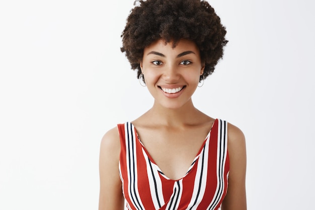 charming friendly-looking African American woman in striped blouse smiling joyfully and gazing polite and carefree