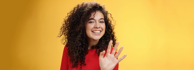 Foto gratuita affascinante donna riccia attraente amichevole e sicura di sé che saluta carina con il palmo per dire ciao o ciao sm