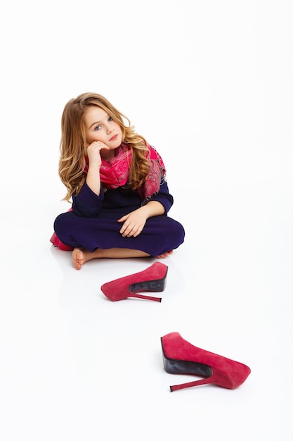 Charming girl in dress sitting on floor in lotus pose with hand on cheek.