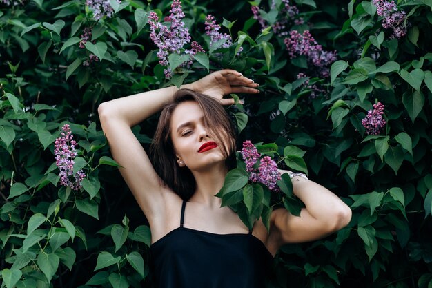 Очаровательная девушка стоит возле кустов с цветами