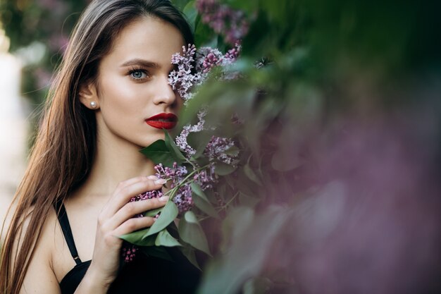 The charming girl stands near bushes with flowers