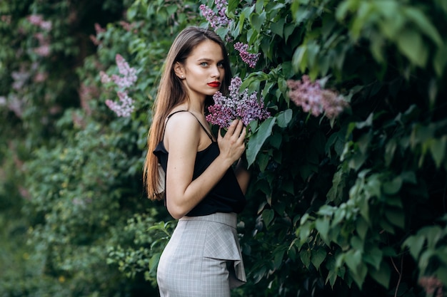 매력적인 여자는 꽃과 덤불 근처에 서