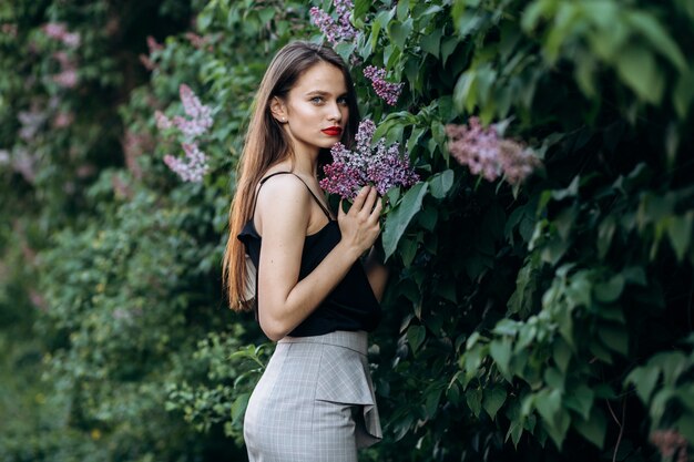 The charming girl stands near bushes with flowers