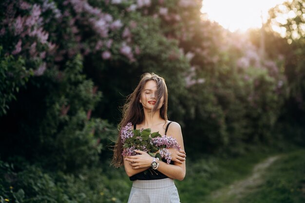 The charming girl stands in the park and keeps a bouquet