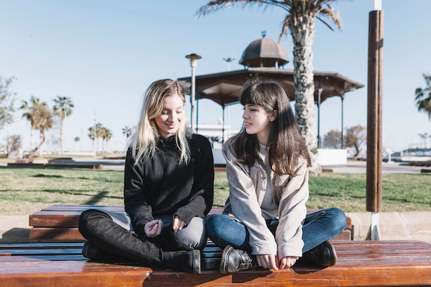 Charming girlfriends chilling in park on bench