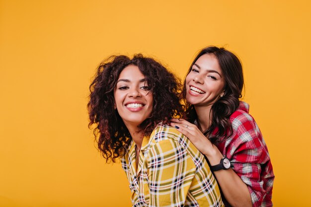 Charming girls in great mood pose for portrait. Lady with clock on hand hugs girlfriend.