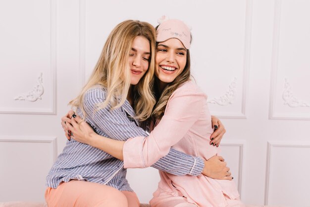 Charming girls in stylish pajamas embracing with smile Indoor shot of wonderful sisters posing in morning