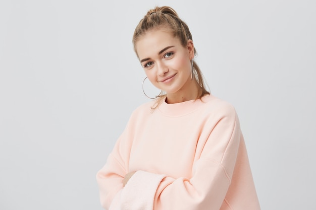 Charming good-looking stylish european girl loking with her dark eyes , smiling , wearing pink sweatshirt with big round earings. Beauty and youth concept.