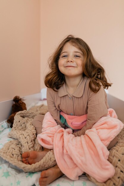 楽しんで、ベッドで遊んでいる魅力的な幸せな少女。家で自由な時間を楽しんでいる小さなきれいな女性の屋内の肖像画