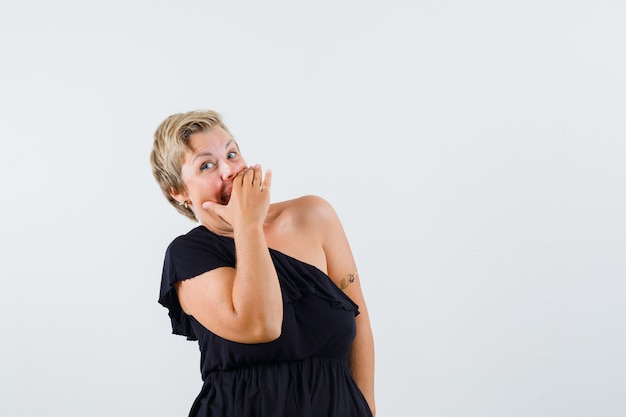 Charming lady in black blouse laughing while holding hand on mouth and looking jolly 