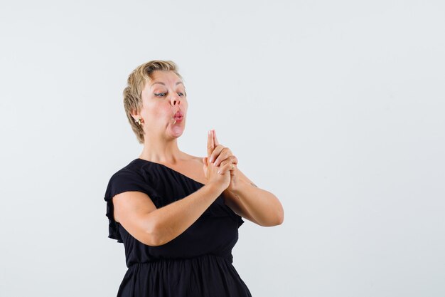 Charming lady in black blouse making pistol gesture and looking confident 