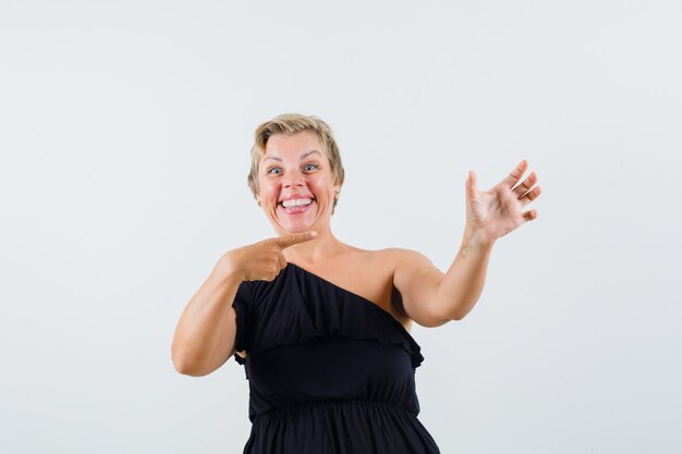 Charming lady in black blouse posing like pointing at phone and looking merry 