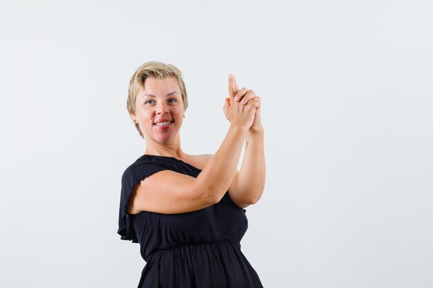 Charming lady making pistol gesture in black blouse front view.