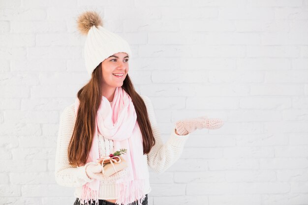 Charming lady in mittens, bobble hat and scarf with present box and opened hand 