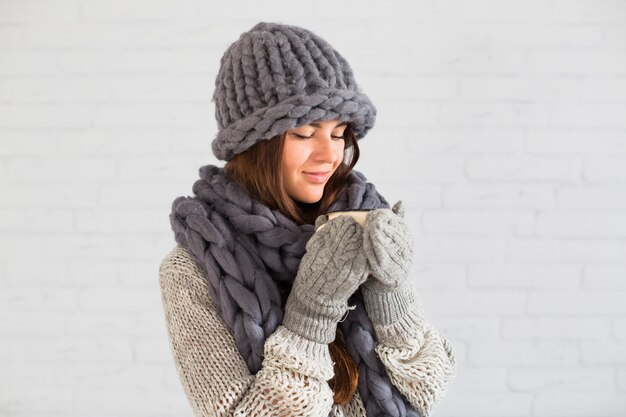 Charming lady in mittens, hat and scarf with cup in hands