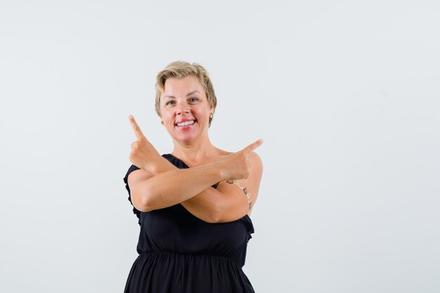 Charming lady pointing at different sides with crossed arms in black blouse and looking hesitant. front view.